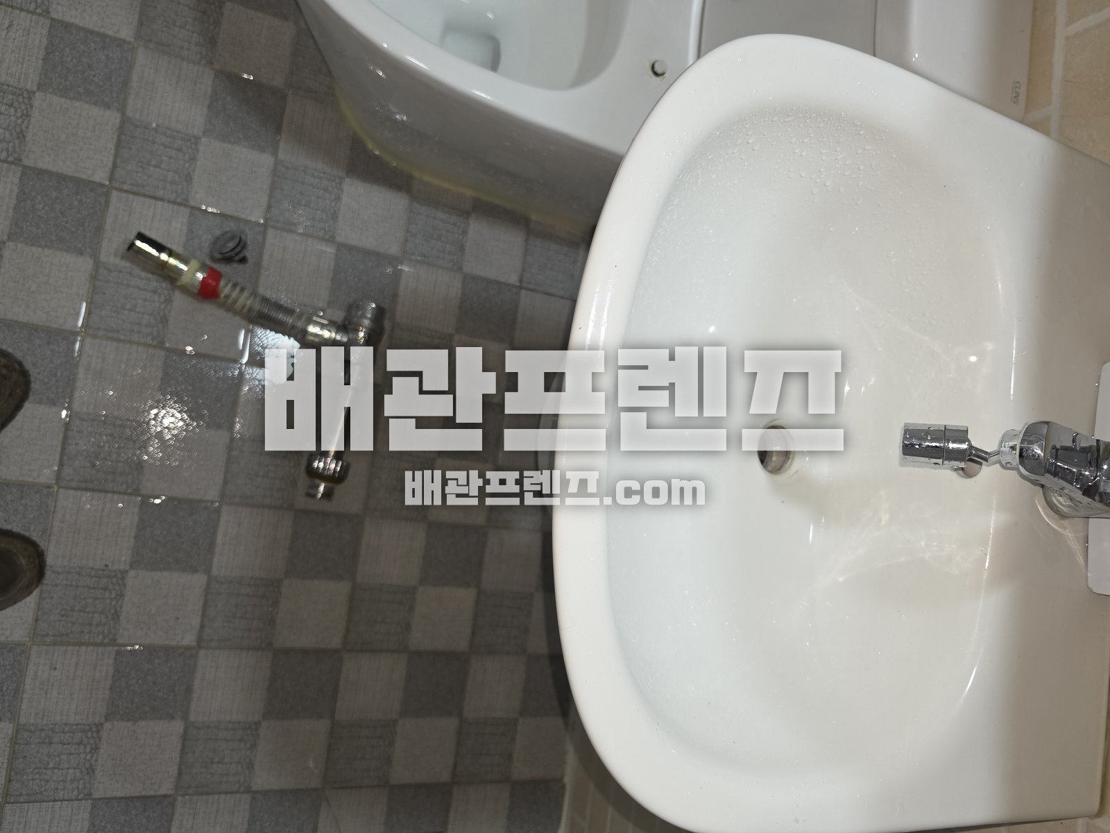 세면대와 바닥 타일 위에 놓인 배수 부속