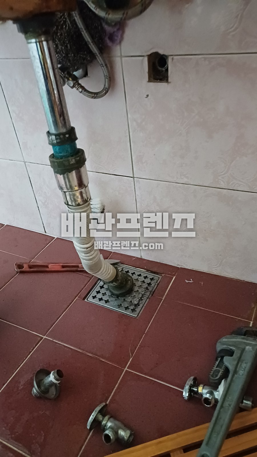벽에서 바닥 배수구로 이어진 배관과 공구