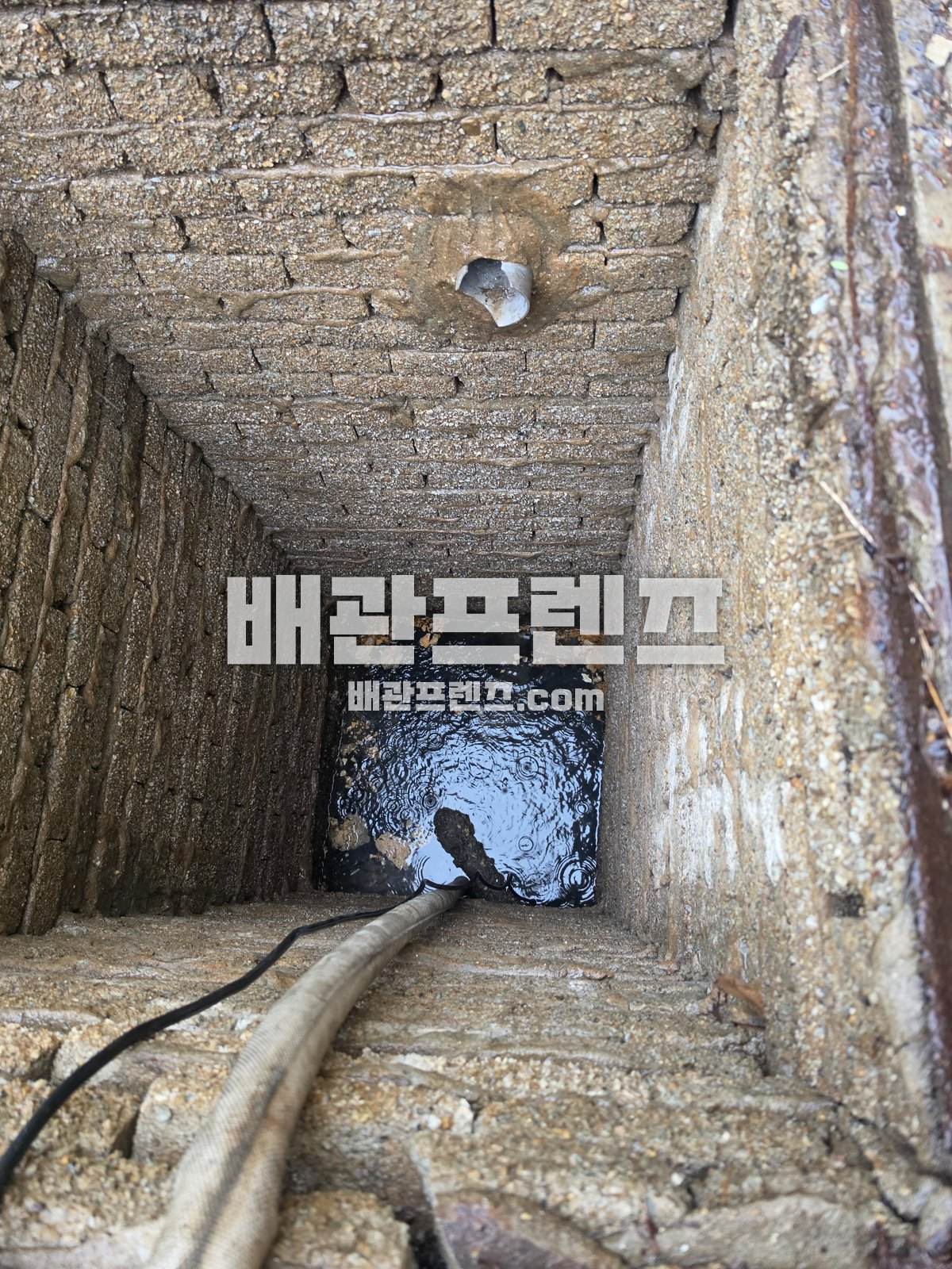 벽돌 집수정 안으로 장비 호스를 넣은 모습