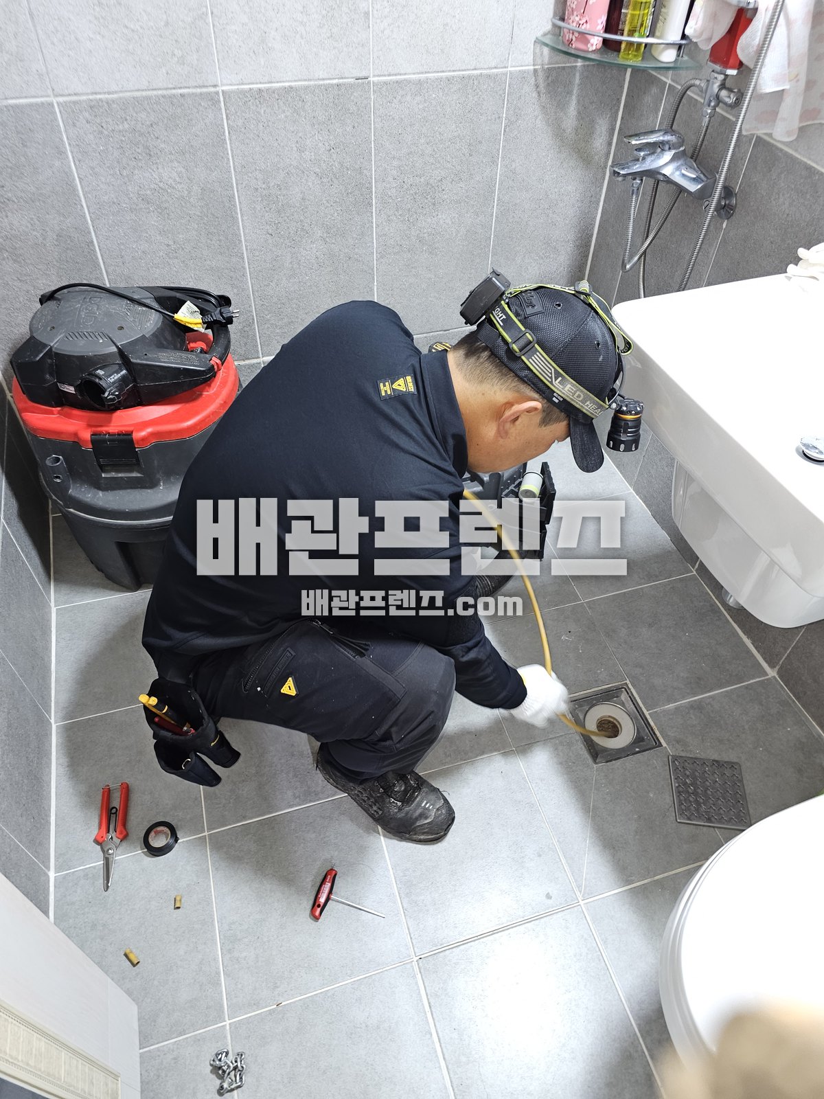 욕실 바닥 배수구에 점검 장비를 넣어 확인하는 작업자