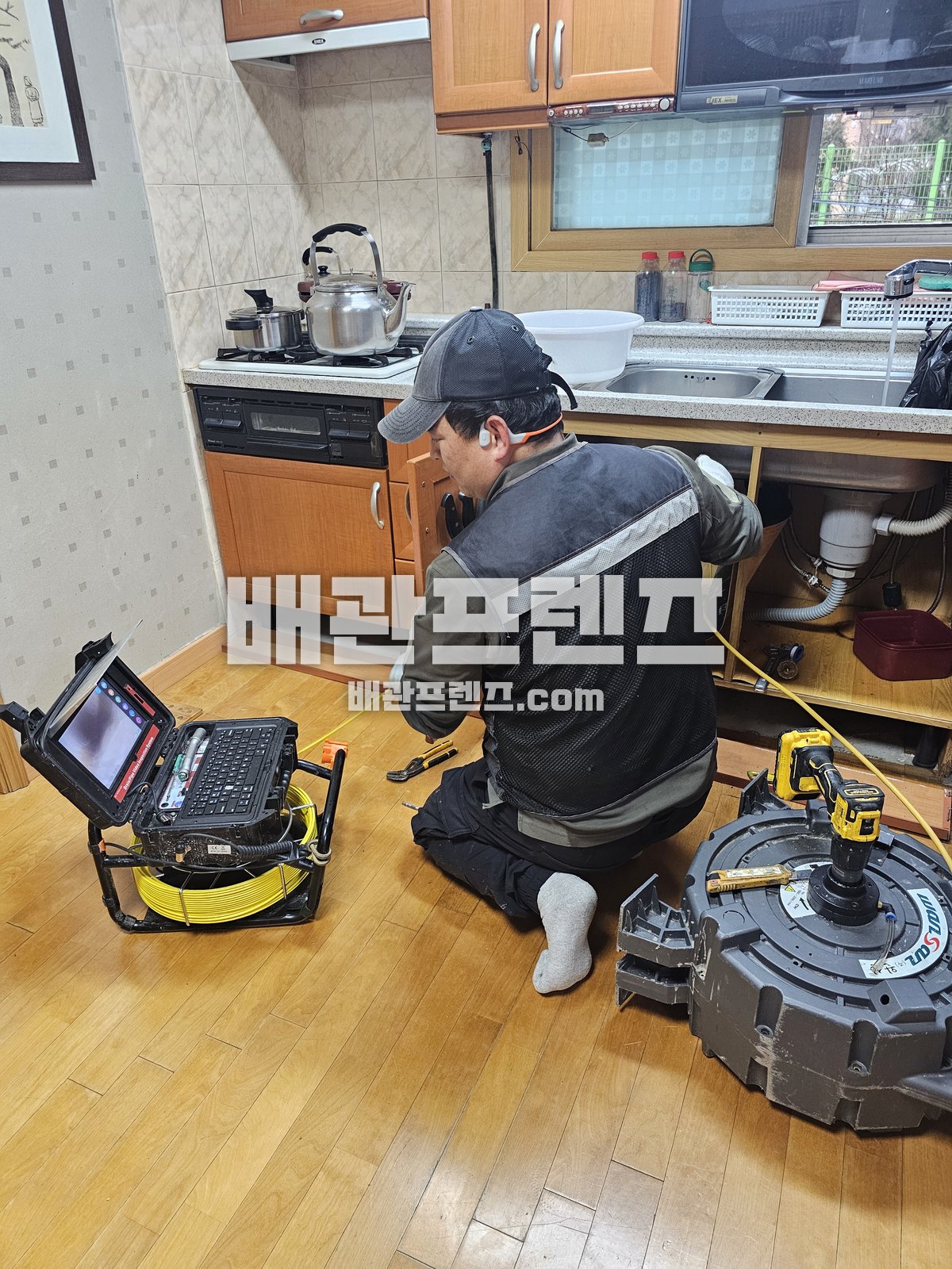 싱크대 아래 배관에 내시경 카메라를 넣고 모니터로 확인하는 작업자