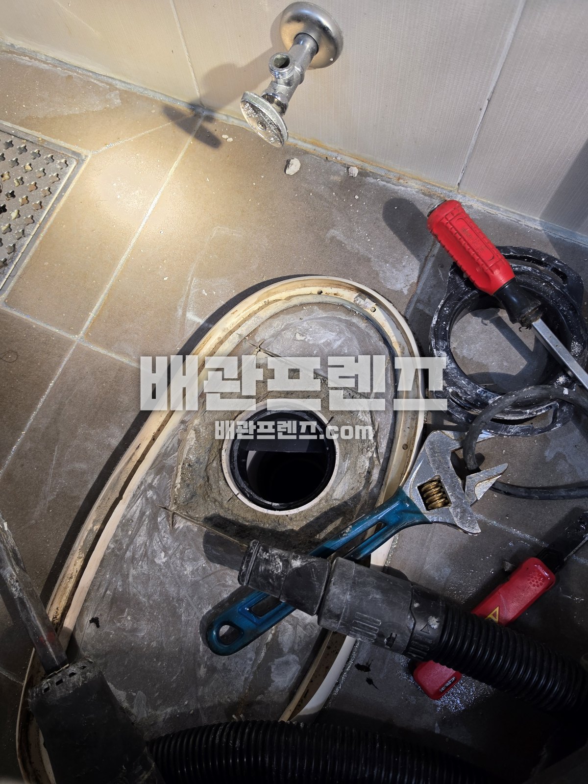 변기를 분리한 욕실 바닥 배관 입구와 옆에 놓인 흡입 호스·공구