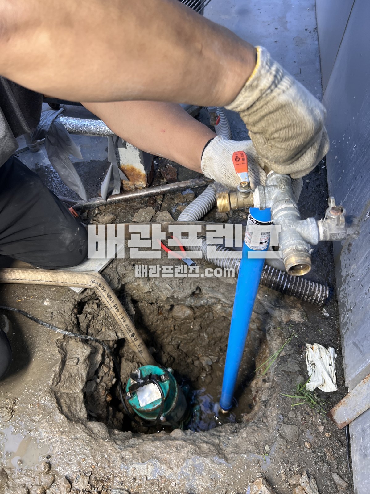 바닥을 열어 드러낸 파란 배관과 금속 밸브 연결부를 작업하는 손