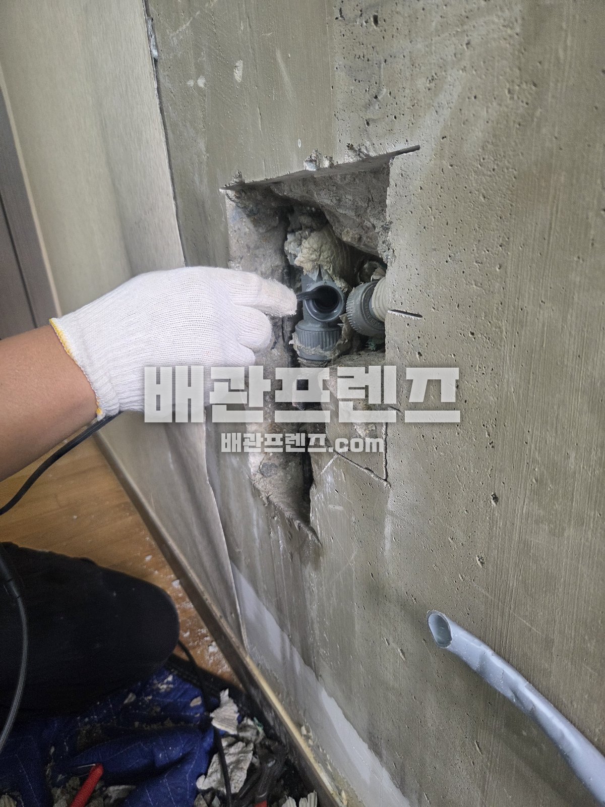 벽을 뚫어 드러낸 배관 연결부를 장갑 낀 손으로 가리키는 모습